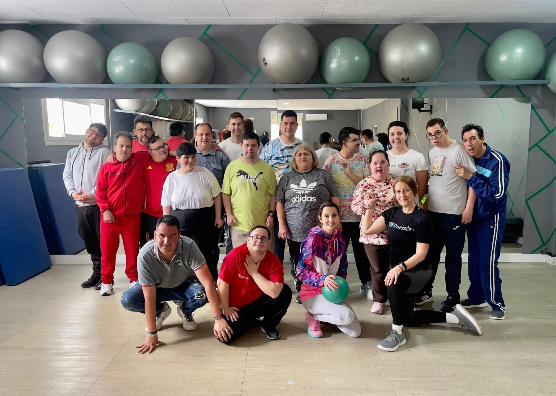 Fotografía real del grupo del Programa posando en una sala de actividad física con grandes pelotas de pilates en una balda superior y suelo de madera clara.